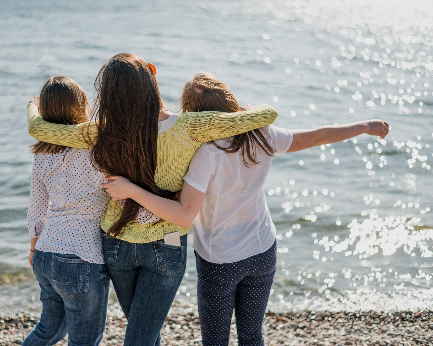 Tres niñas abrazadas miran juntas hacia el mar